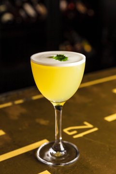 A yellow cocktail in a nick and nora glass garnished with cilantro at the bar