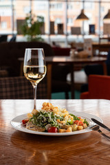 Caesar salad with white wine served on wooden table in a restaurant