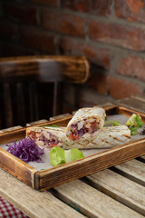 Grilled roll shawarma with chicken breast, tomatoes and red cabbage served on wooden tray