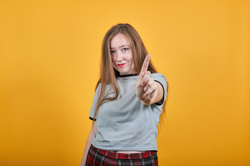 Attractive caucasian young girl over isolated orange wall wearing fashion clothes keeping fingers directly, opened eyes, smiling
