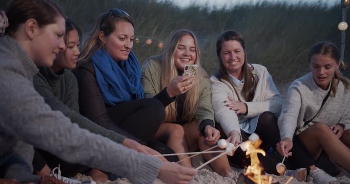 Girlfriends having a good time around campfire on the beach. Cinematic lifestyle scene perfect for travel or corporate video projects.