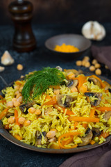 Vegetarian pilaf with mushrooms, vegetables and chickpeas on a black concrete background. Vertical photo.