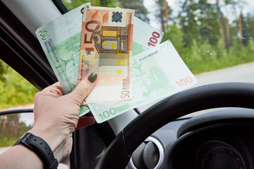 Euro banknotes of various denominations in a woman hand inside of a car