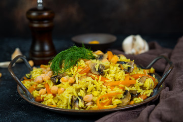 Vegetarian pilaf with mushrooms, vegetables and chickpeas in the center on a black concrete background.