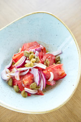 Salad of colorful tomatoes, olives, capers and basil. Wooden table in restaurant