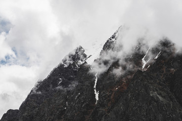Atmospheric minimalist alpine landscape with hanging glacier on snowy rocky mountain peak. Low clouds among snowbound mountains. Serac on glacial edge. Majestic misty foggy scenery on high altitude.