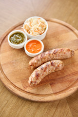 Grilled sausages. Serving on a wooden Board. Barbecue restaurant menu, a series of photos of different meats. Pickled cabbage and two sauces