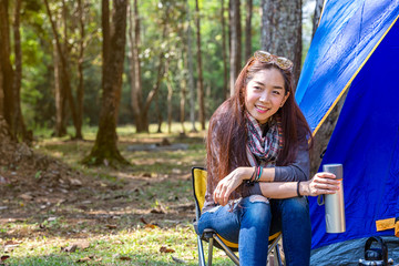 Tourists camping in the forest. Asian female camping and backpack travel sitting relax alone in forest. Drink water for refreshing active at morning having lifestyle nature mountain in forest.