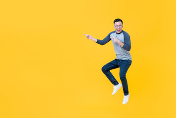 Fototapeta na wymiar Casual smiling Asian man jumping and pointing fingers to copy space aside