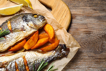 Delicious roasted fish and potatoes on wooden table, flat lay