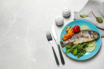 Delicious roasted fish with lemon and vegetables on grey marble table, flat lay. Space for text