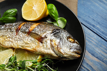 Delicious roasted fish with lemon on blue wooden table, closeup