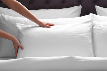 Woman fluffing white pillow on bed, closeup