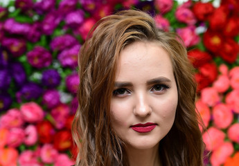 Obraz na płótnie Canvas The concept of beauty, fashion, makeup, cosmetics. Portrait of a pleasant young pretty brunette girl with a beautiful hairstyle, great makeup, long curly hair against a background of flowers.
