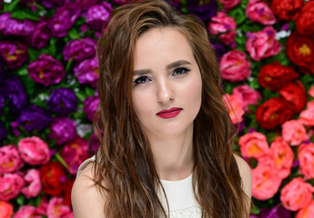 Fototapeta premium The concept of beauty, fashion, makeup, cosmetics. Portrait of a pleasant young pretty brunette girl with a beautiful hairstyle, great makeup, long curly hair against a background of flowers.