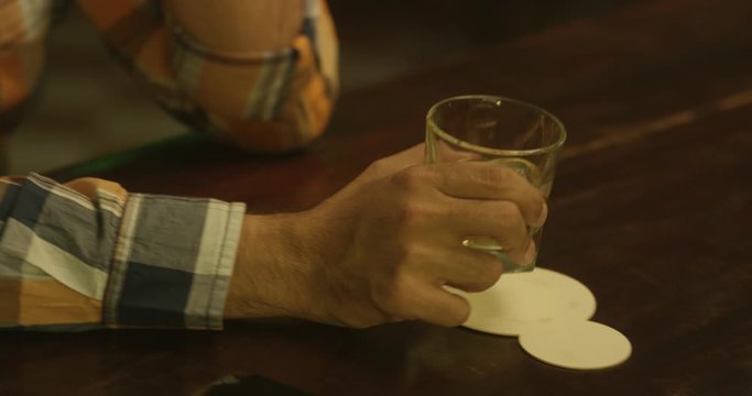 A bartender serving a whiskey in a glass to a sad man at the counter. Handheld detail shot.