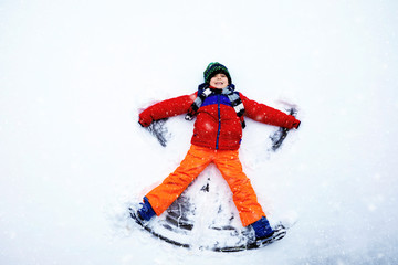Fototapeta na wymiar Cute little kid boy in colorful winter clothes making snow angel, laying down on snow. Active outdoors leisure with children in winter. Happy healthy child having fun and laughing outdoors