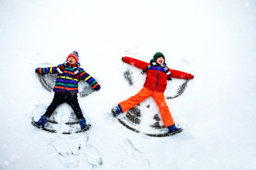 Fototapeta na wymiar Two little siblings kid boys in colorful winter clothes making snow angel, laying down on snow. Active outdoors leisure with children in winter. Happy brothers with warm hat, gloves, winter fashion.