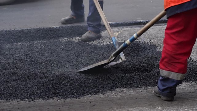 Workers on a road construction, industry and teamwork. Fresh asphalt construction. Bad road. Roller and workers on asphalting and repair of city streets. Close-up.