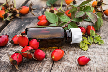 Bottle of rosehip seed essential oil and fresh red berries on a wooden table. Tincture or essential oil with rose hips.