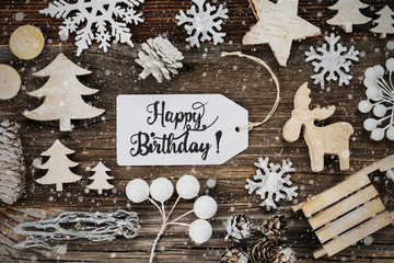 Obraz na płótnie Canvas One White Label With English Text Happy Birthday. Frame Of Christmas Decoration Like Tree, Sled, Star And Fir Cone. Wooden Background With Snowflakes