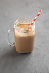 Homemade smoothie with coffee, oat and banana in a glass jar mug on a gray surface, low angle view. Close-up.