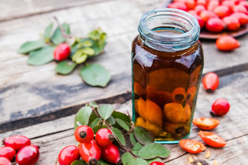 Tincture or drink with wild rose in a glass bottle near ripe red rosehip berries.