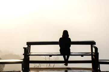 The image behind Woman sitting on a wooden chair Background fog  and morning sunlight.