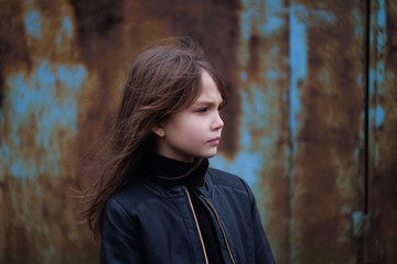 serious young girl in a black leather jacket against a rusty wall