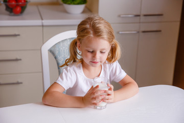  little girl sits at home at the kitchen table and drinks milk for breakfast	