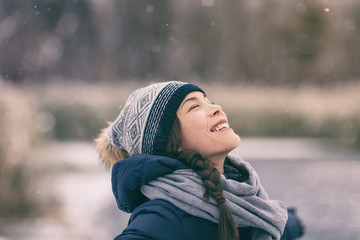 Fototapeta Winter woman happy enjoying snow falling on face outdoor forest nature Asian girl looking up wearing hat and scarf cold weather clothes. obraz