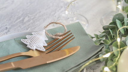 Nordic Festive tableware for Christmas and New Year celebration. Close up  of Gold cutlery and green linen napkin on cement background. Kinfolk style