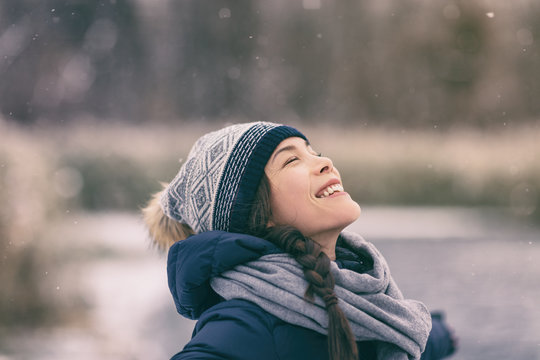 Winter Woman Happy Enjoying Snow Falling On Face Outdoor Forest Nature Asian Girl Looking Up Wearing Hat And Scarf Cold Weather Clothes.