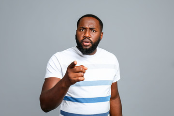 Troubled African-American man pointing at viewer on grey background