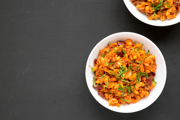Homemade Chili Mac and Cheese with Parsley in white bowls over black surface, top view. Flat lay, overhead, from above. Space for text.