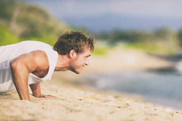 Fit man training on beach doing push-ups workout summer fitness lifestyle.