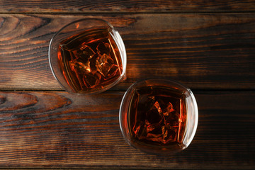 Glasses of whiskey with ice cubes on wooden background, top view