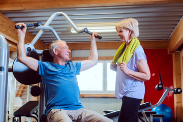 Fototapeta na wymiar Senior man in the gym with his wife on exercise machines
