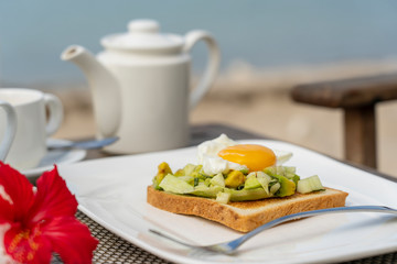 Healthy sandwich with avocado, cucumber and poached eggs on table for healthy breakfast on the beach near sea. Food and breakfast concept.