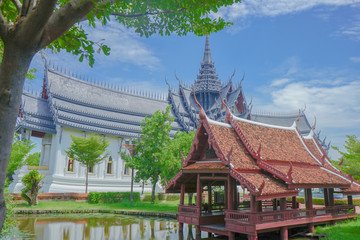ancient city museum reproduce of traditional heritage east tropical Thai style pavilion in water pond and grey grand palace temple architecture which has multiple roof layers and spire on the top.