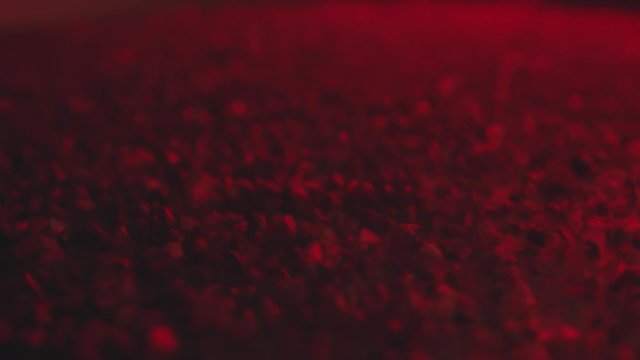 Black stones shaking and moving through vibrations of sound. Natural coals, macro shot. Camera tilting down. Moden red neon light.