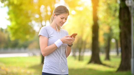 Girl athlete jogging in the evening park. Resting and talking on social networks. Listening to music. Workout. Healthy lifestyle.