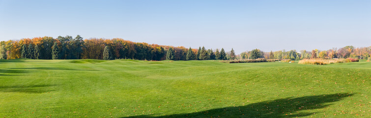 Panoramic view of large lawn against autumn forest and sky