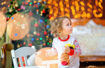 cute baby in pajamas plays in a festively decorated room, against the background of bright lights