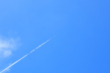 Small white plane with white smoke trail on the blue sky.