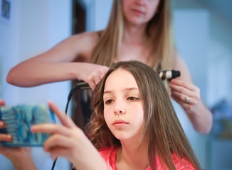 Beautiful woman curls long hair to the girl using curling iron