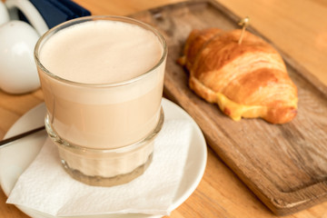A Cup of cappuccino and a hot croissant on a wooden table