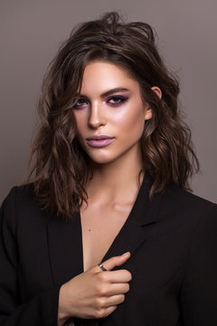 Portrait of young beautiful brunette model with violet professional make up, trendy wavy hairdo and perfect skin.