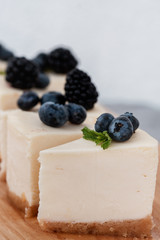 sliced cheesecake on a wooden board with blueberries and blackberries on a gray background. classic cheesecake new york