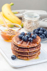 Healthy oatmeal banana pancakes garnished with blueberry and honey, on white board, vertical
